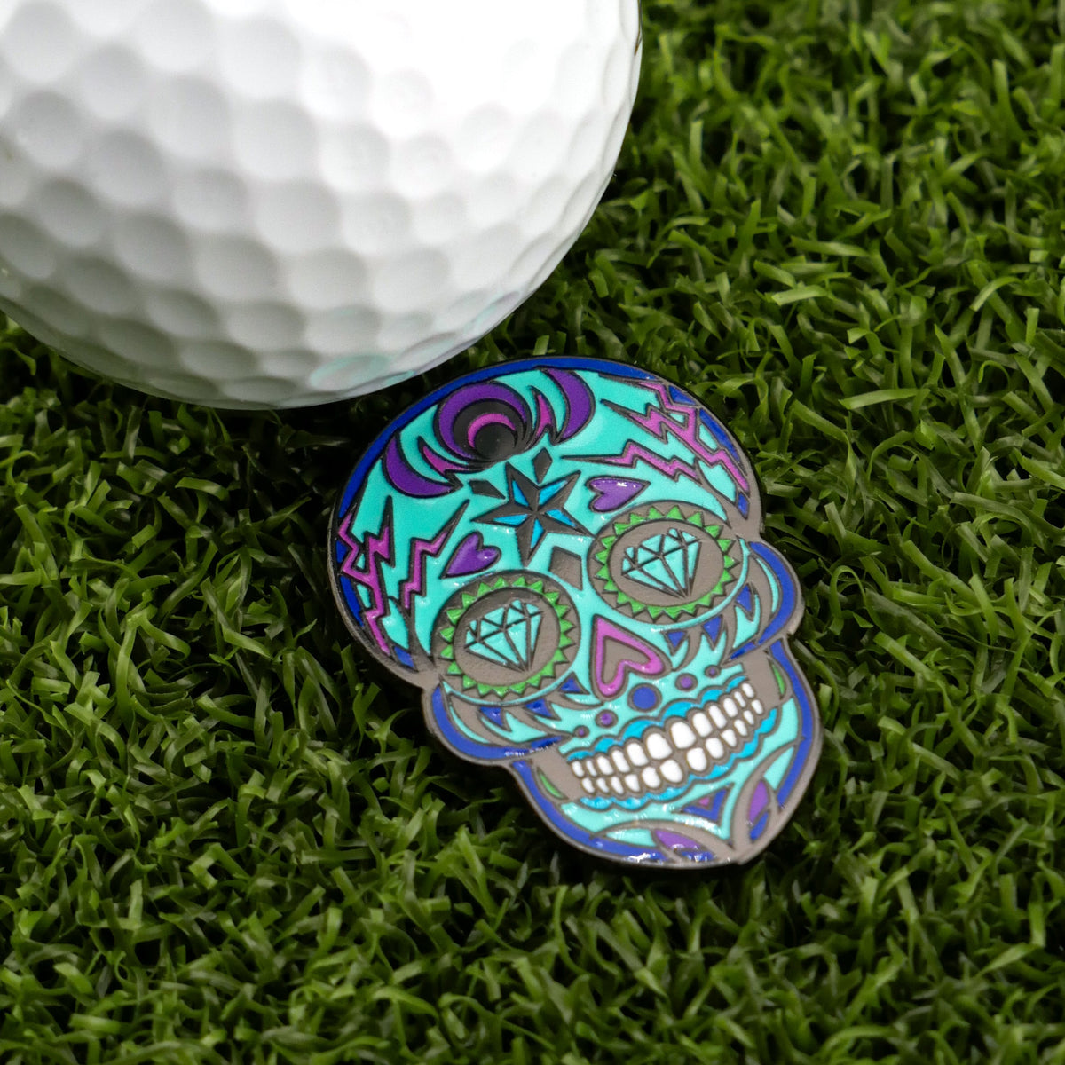 Blue sugar-skull ball marker beside a golf ball on turf