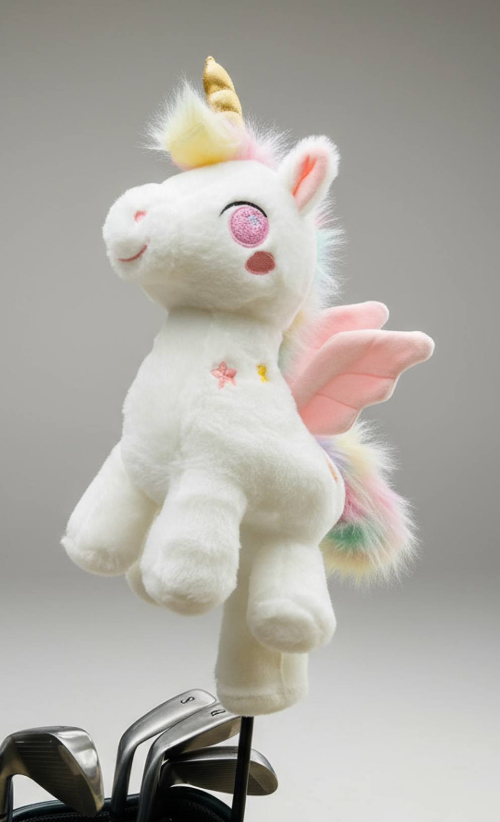 Plush unicorn golf club headcover with pink wings and a yellow horn perched on golf club heads