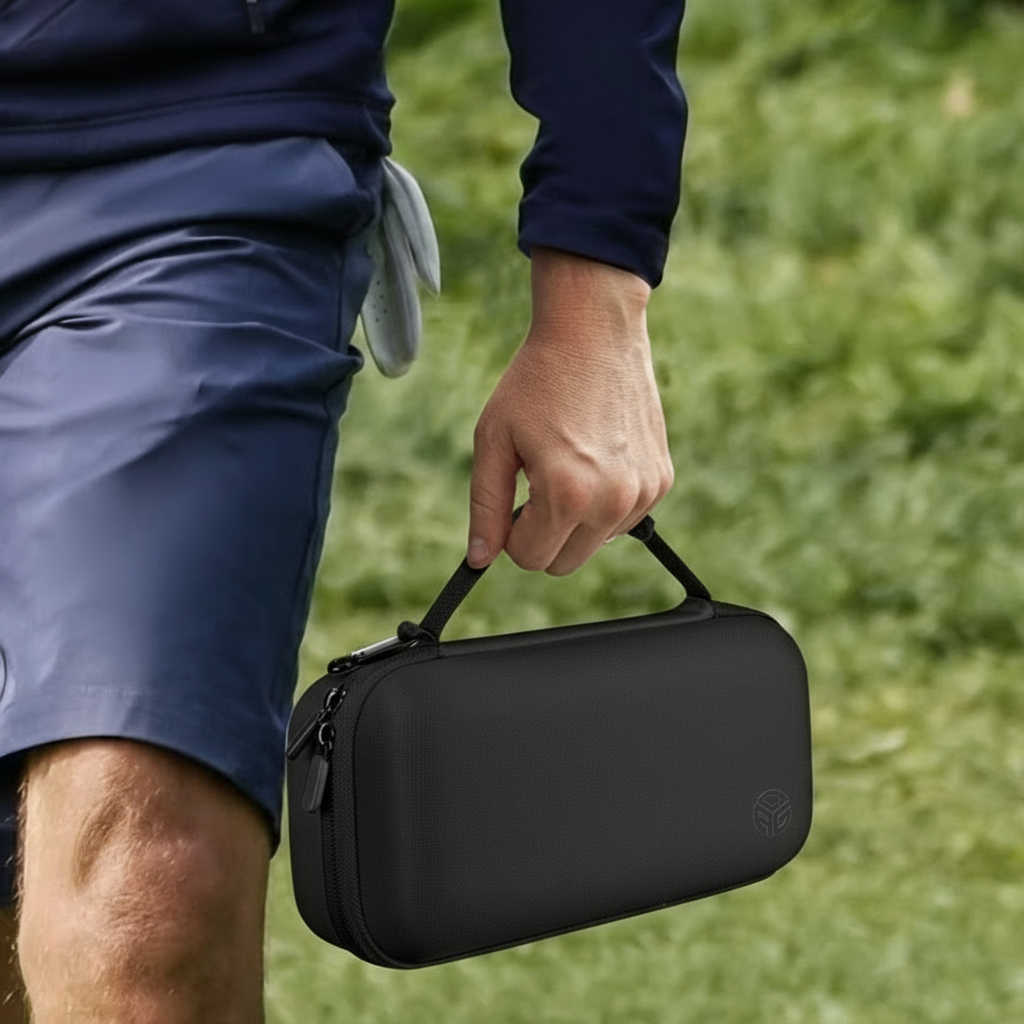 Person holding a black carrying case with a logo on grass