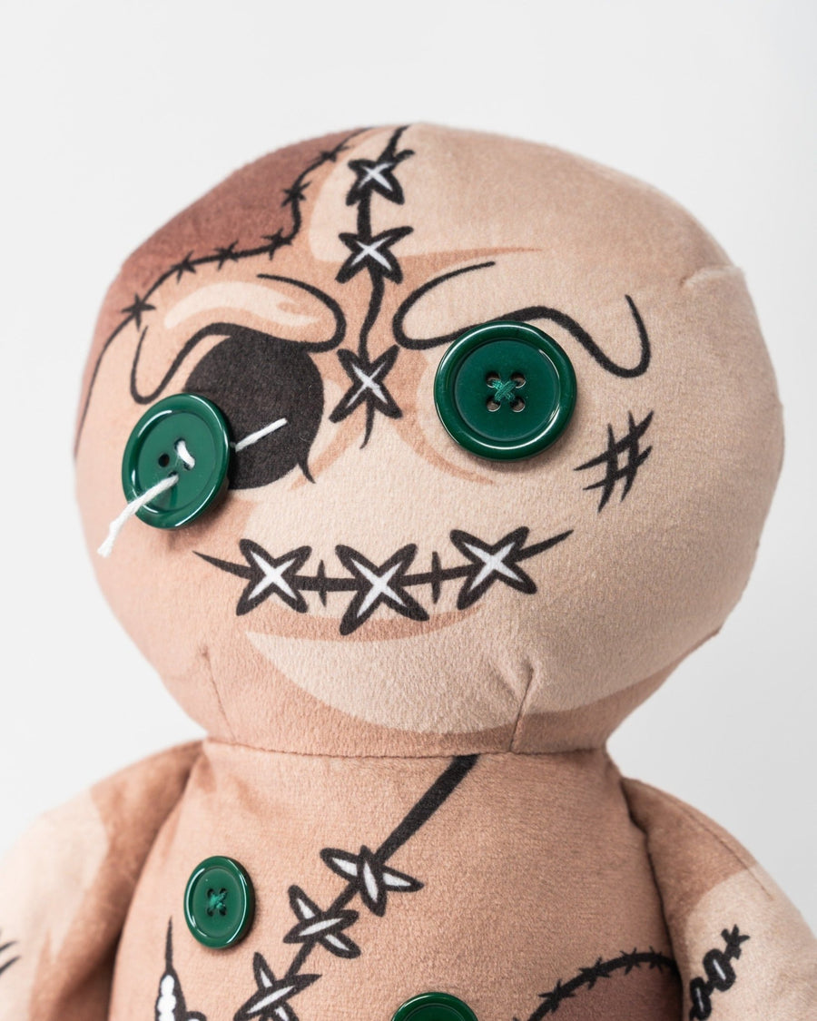 Close-up of the tan voodoo doll cover with green button eyes and stitched-face graphics