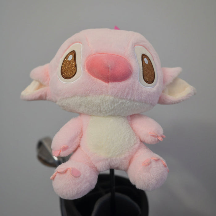 A pink plush toy with large brown eyes and a pink nose, resembling Stitch, sitting on a black stand against a textured beige wall.