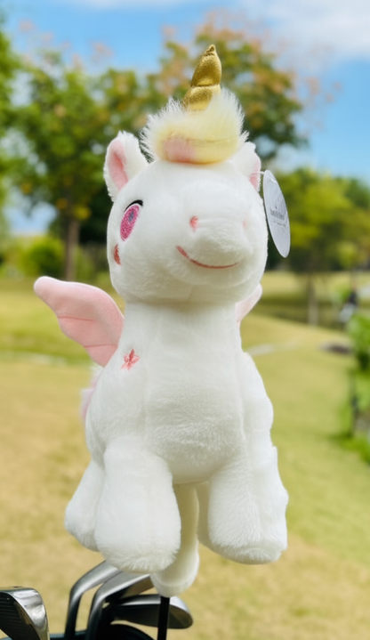 Plush unicorn golf club headcover with pink wings and a golden horn perched on a golf club against a green outdoor background