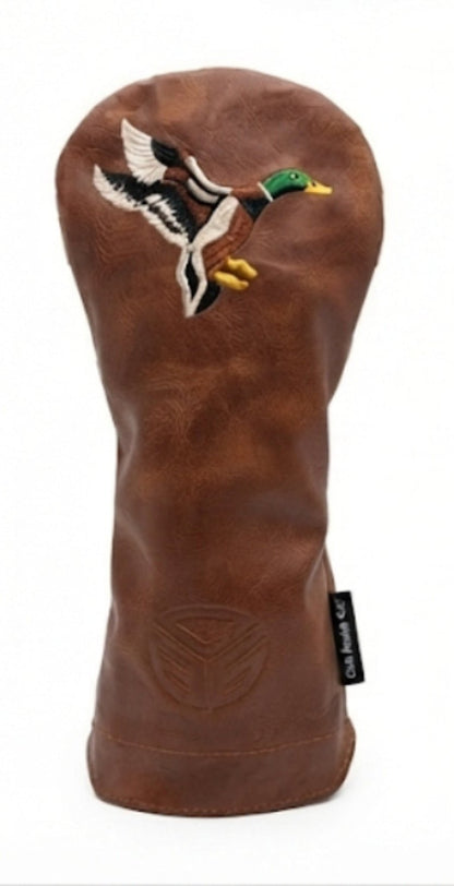 A brown leather golf club headcover featuring an embroidered mallard duck in flight on the front, with a small black brand tag on the lower right.