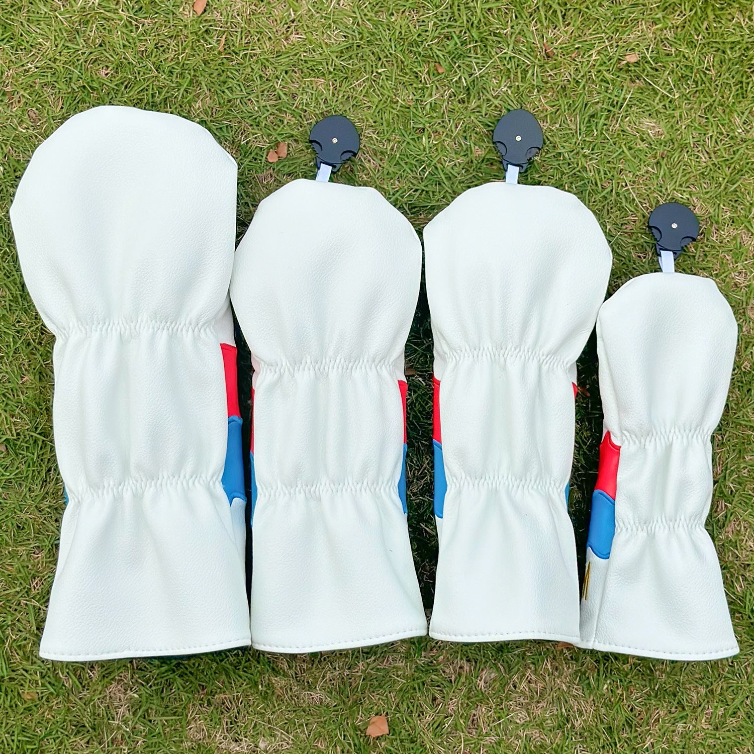 Four white golf club heads with blue and red accents on a grass background