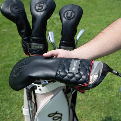 Close-up of golf clubs with black grips held by a person on a grassy background