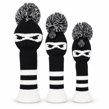 Three black-and-white ninja knit golf headcovers with pom-poms on a white background