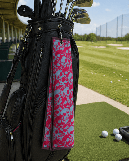 Golf bag with pink and blue skull patterned towel on a golf course