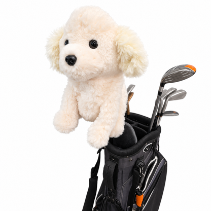 A cream-colored plush dog toy with black eyes and nose sits on top of a black golf bag containing golf clubs, isolated on a white background.