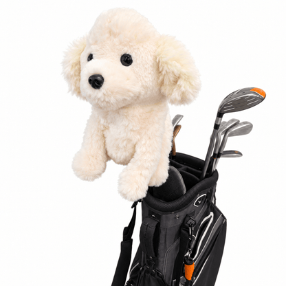 A cream-colored plush dog toy with black eyes and nose sits on top of a black golf bag containing golf clubs, isolated on a white background.