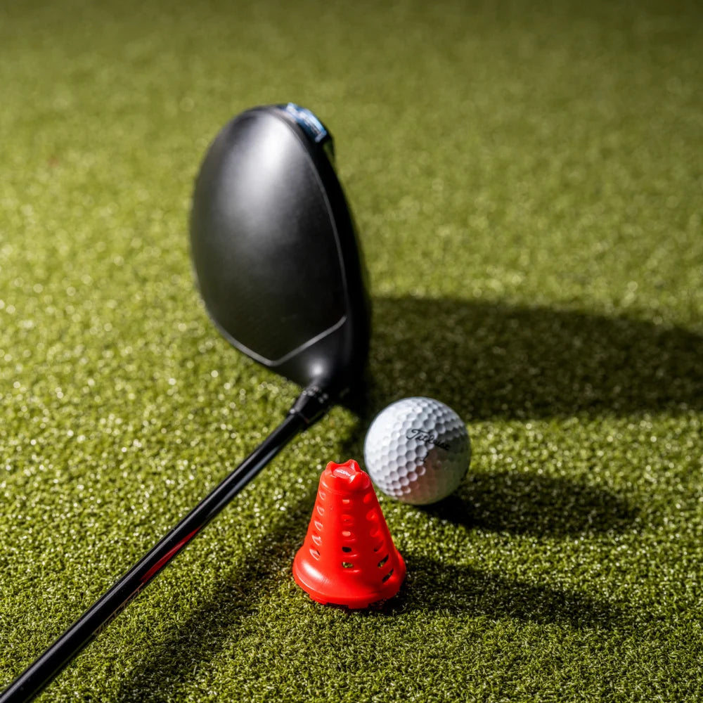Red simulator golf tee on turf beside a driver and golf ball.