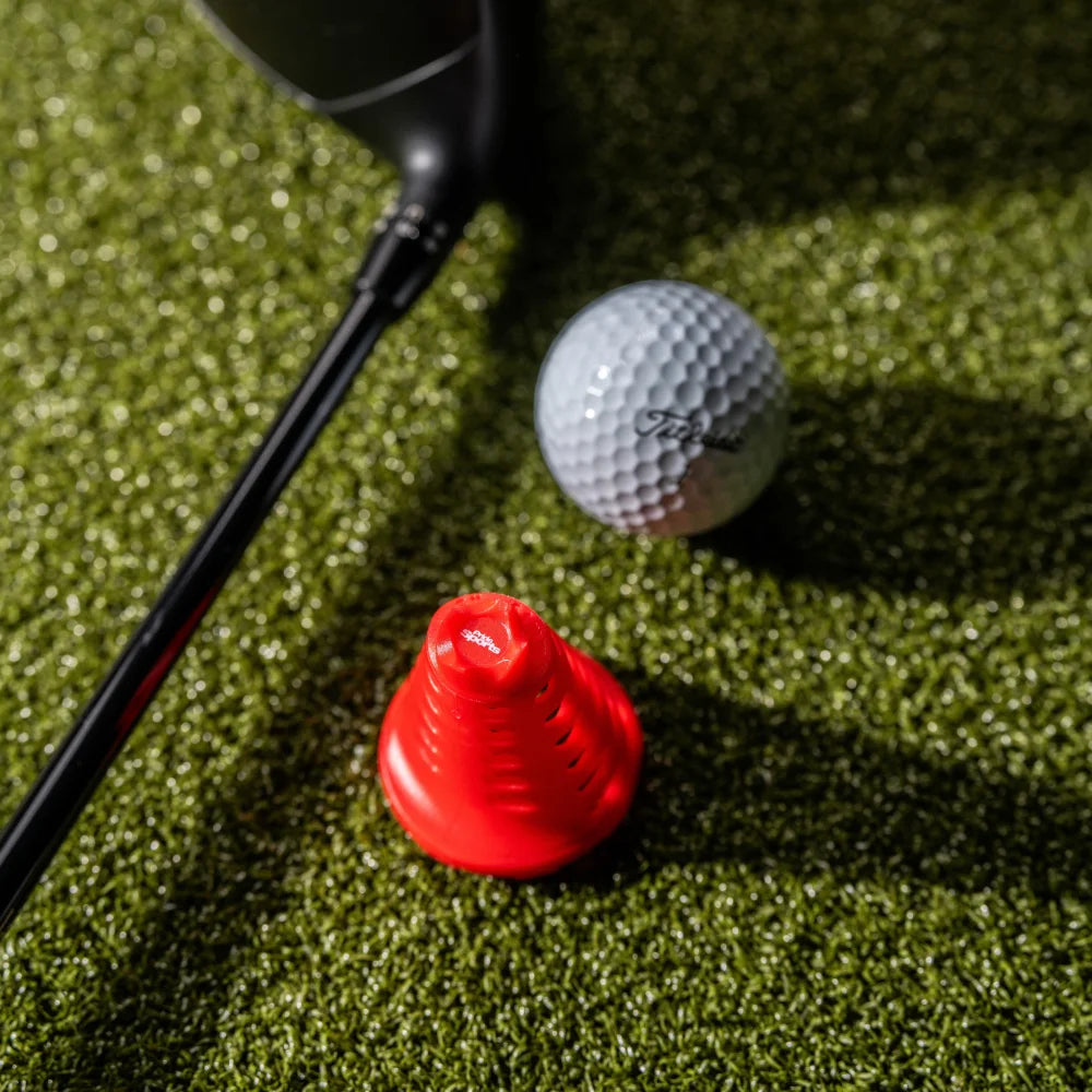 Close-up of red Pride Sports simulator golf tee next to driver head and ball.