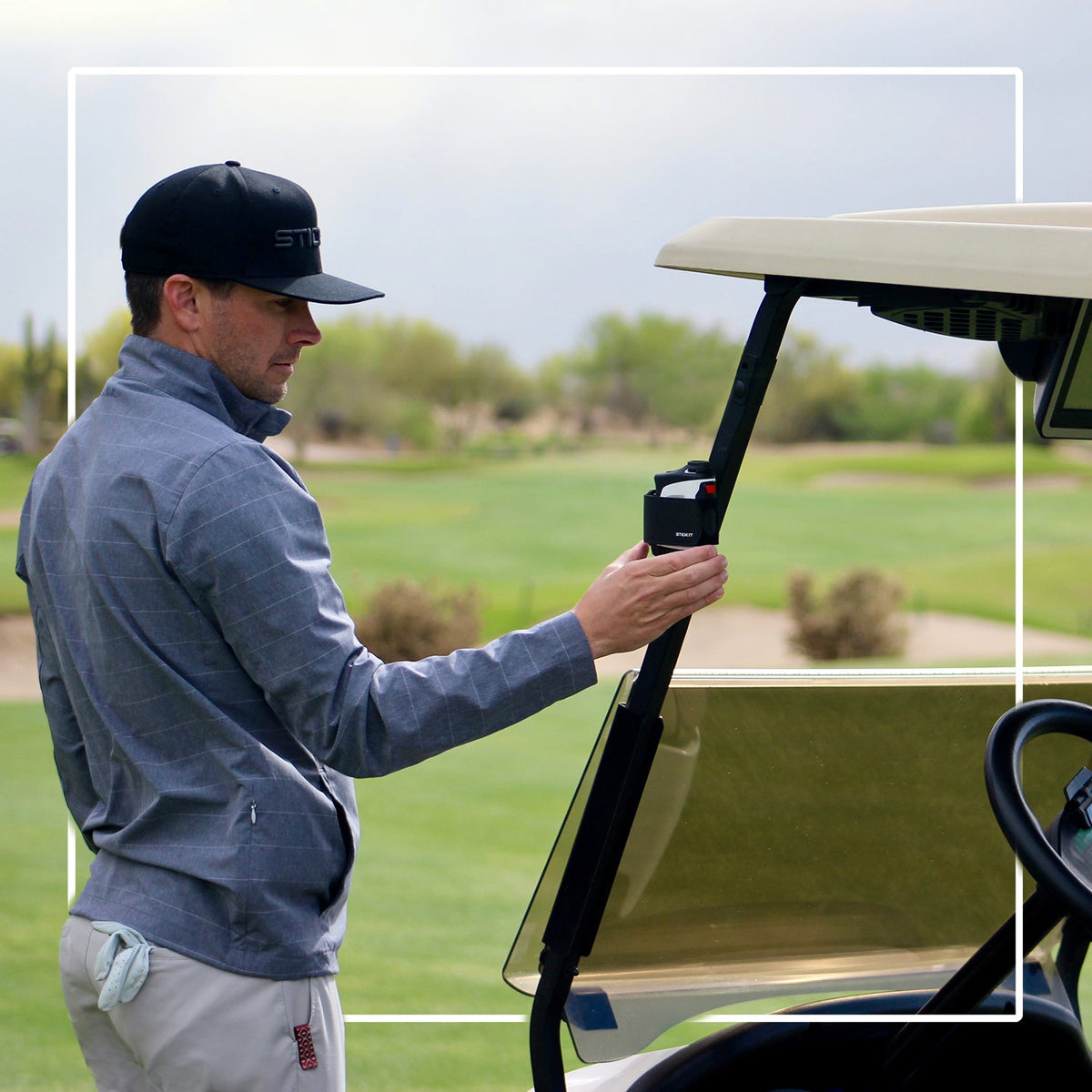Golfer retrieving a rangefinder with a black STICKIT Gen3 strap from a metal cart post; rangefinder not included