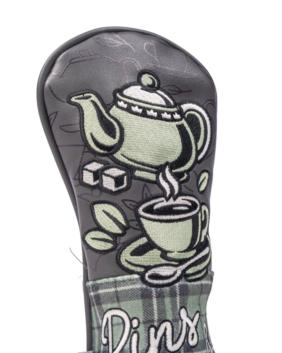 Embroidered teapot, steaming cup and sugar cubes above gray-green tartan on the hybrid cover