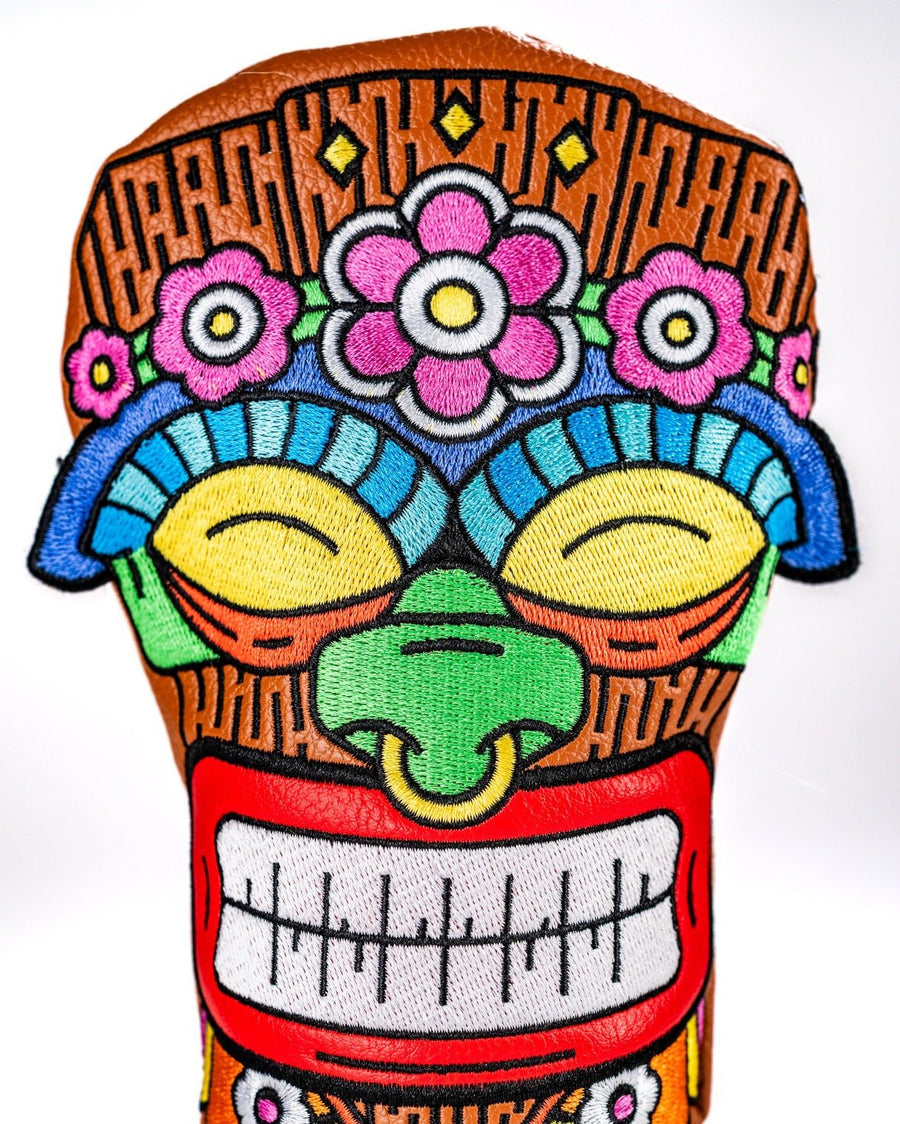 Smiling tiki hybrid face with pink flowers, yellow eyes, green nose and a red-bordered grin