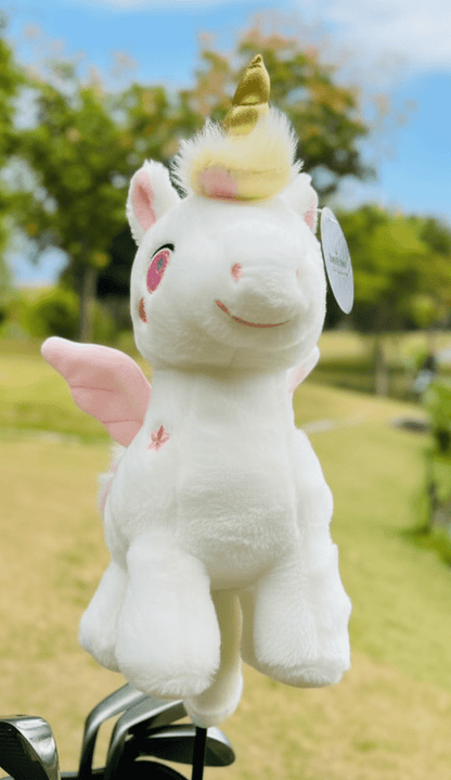Plush unicorn golf club headcover with pink wings and a golden horn perched on a golf club against a green outdoor background