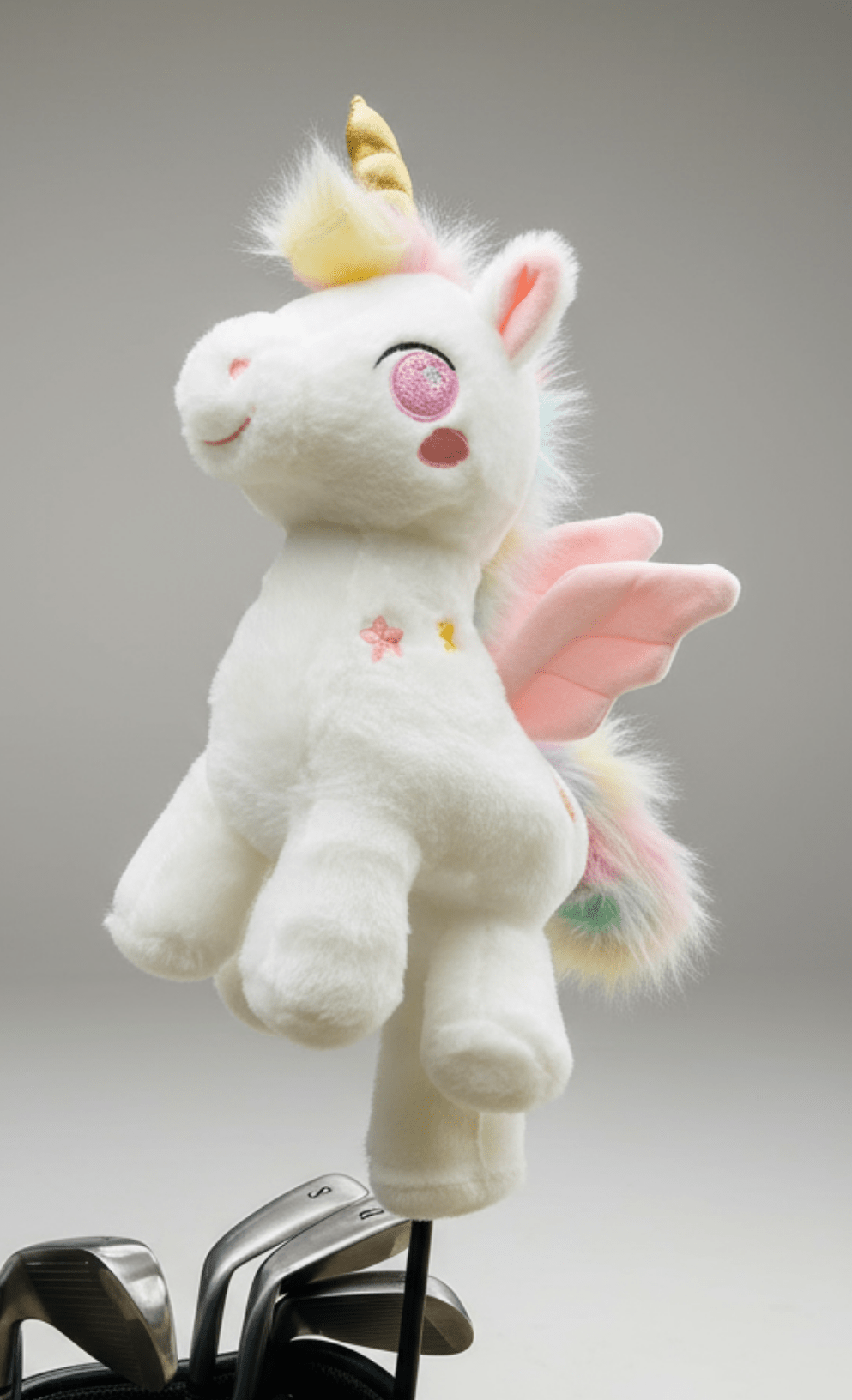 Plush unicorn golf club headcover with pink wings and a yellow horn perched on golf club heads